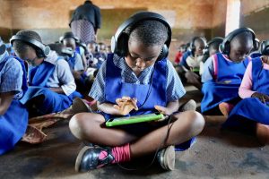 
A child in Malawi sits on the classroom floor and learns through an electronic tablet. 